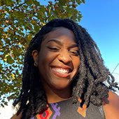 Alexis Moise stands outside, under a tree, smiling at camera